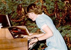 A young woman bends over an organ console.  A Christmas tree on the right side of the console fills the background. - , Utah